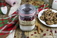 a glass jar filled with cookies and cranberries next to a plate of cookies