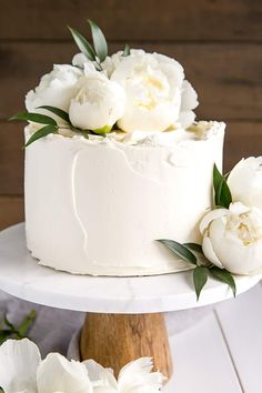 a white cake with peonies and greenery on top is displayed for instagram