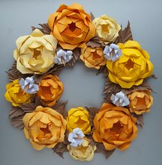 an origami wreath made out of yellow and orange paper flowers on a gray background