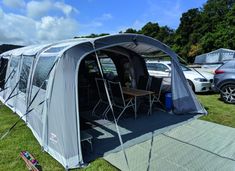 an awning tent is set up in the grass next to parked cars and picnic tables