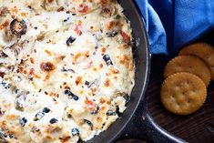 a skillet filled with cheese and olives next to crackers