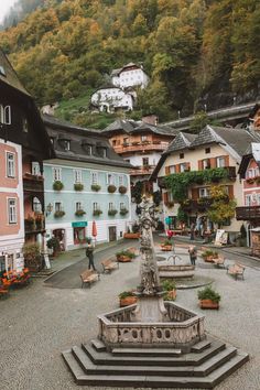 a fountain in the middle of a town square with buildings on both sides and mountains in the background