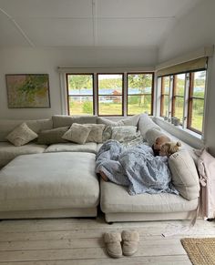 a person laying on top of a white couch in a living room next to two windows