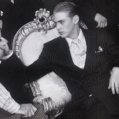 black and white photograph of two men in suits sitting on a chair with one holding the arm of another man's hand