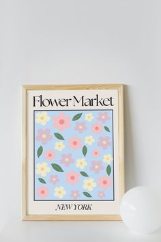 a flower market poster hanging on the wall next to a white vase with flowers in it