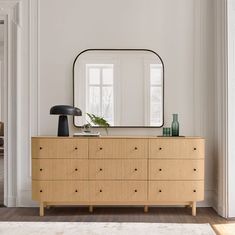 a dresser with a mirror and vases on it in a white living room area