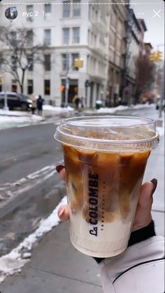 someone holding up a cup of iced coffee on the sidewalk in front of some buildings