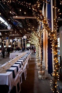 tables and chairs are set up for an event with white tablecloths and lights hanging from the ceiling