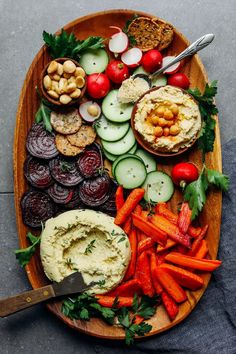 a platter with carrots, radishes, cucumbers and hummus