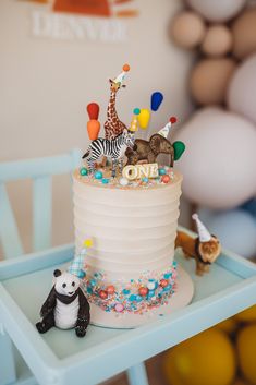 a birthday cake with animals and balloons on the top is sitting on a small table