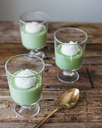 three glasses filled with green pudding on top of a wooden table next to a spoon