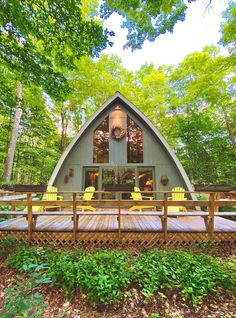 a wooden deck with yellow chairs on it in front of a small cabin surrounded by trees