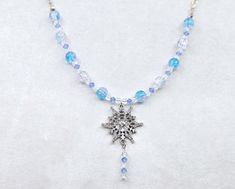 Embrace the magic of winter with this captivating necklace, featuring a shimmering snowflake pendant suspended from a delicate sterling silver chain. The pendant is accompanied by a chain of frosty blue and white crackle glass beads, evoking the beauty of snow and ice. Each crackle bead catches the light, creating a sparkling effect reminiscent of frozen landscapes. Perfect for adding a touch of wintry elegance to any outfit, this necklace captures the serene beauty of the season, making it a st Snowflake Pendant, Crackle Glass, White Necklace, Crystal Drop, Glass Necklace, Blue Crystals, Sterling Silver Chain, Sterling Silver Chains, Silver Chain