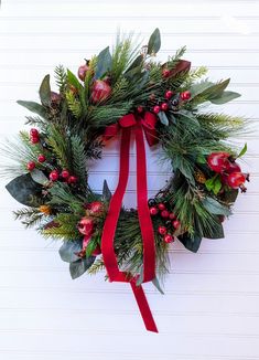 a christmas wreath hanging on the side of a building with red ribbon and evergreen leaves