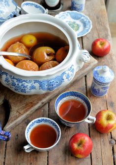 two cups of tea and some apples on a wooden table next to an old pitcher