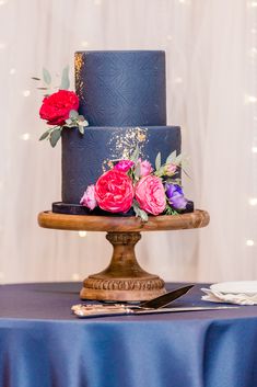 a three tiered blue wedding cake with pink and red flowers