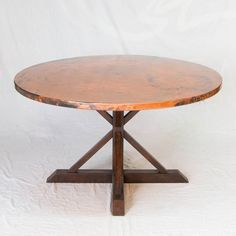 a round wooden table sitting on top of a white background with an iron cross base