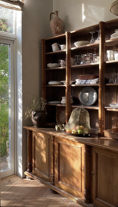 a wooden cabinet with dishes on it in front of a sliding glass door that leads to an outside patio