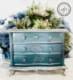 a blue dresser with flowers in front of it on a white tableclothed surface