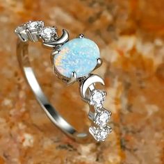 a white opal and diamond ring sitting on top of a marble surface with a stone background