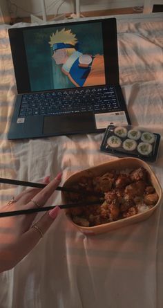 a person holding chopsticks in front of a bowl of food on a bed