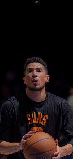 a man holding a basketball in his right hand while wearing a black shirt with suns on it