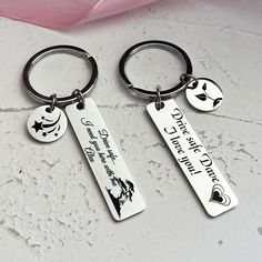 two keychains with different designs on them sitting next to a pink flower and ribbon