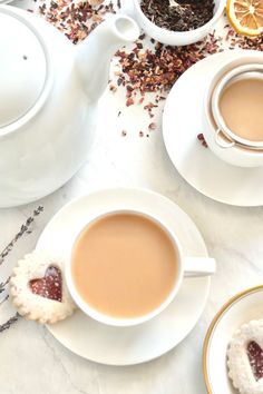 two cups of tea and some cookies on a white table with orange slices, lemon wedges and dried herbs