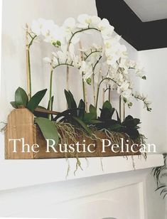 the rustic pelican logo is displayed on a fireplace mantel with white orchids and greenery