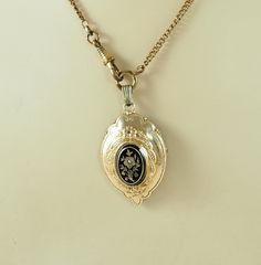 A charming antique Victorian locket back shield shaped pendant with a 14K gold front with black enamel and seed pearl. The center with an oval black enamel panel with a very lovely gold rose of Sharon or possibly a pansy flower and foliage set with a seed pearl, 1mm in diameter, with a gold band and black enamel outer border. With embossed trailing husks and forget-me-not. With a finely beaded outer border. The reverse in acid tested silver with a glazed opening panel and the remains of the orig Victorian Engraved Rose Gold Locket Necklace, Victorian Cameo Locket Necklace For Formal Occasions, Antique Black Engraved Jewelry, Formal Victorian Hallmarked Locket Necklace, Victorian Rose Gold Locket Necklace, Antique Oval Jewelry With Black Enamel, Victorian Pendant Locket Necklace For Formal Occasions, Antique Oval Black Enamel Jewelry, Formal Antique Necklace With Black Enamel