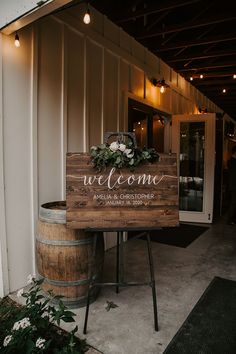 a welcome sign sitting on top of a wooden barrel next to a building with lights