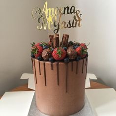 a chocolate cake with strawberries and blueberries on top is decorated with gold lettering