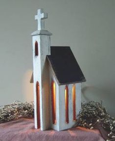 a small white church sitting on top of a red and white table cloth next to a candle