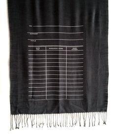 a black scarf with white writing on it and fringes hanging from the end of it