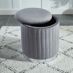 a round stool with a cushion on the floor in front of a white rug and wall