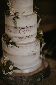 a three tiered cake with flowers and greenery on the top is sitting on a tree stump