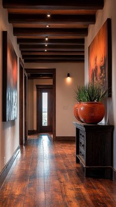 a long hallway with wooden floors and paintings on the wall, along with a plant in an orange vase