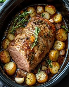 a pork roast with potatoes and rosemary garnish in a slow cooker, ready to be eaten