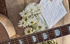 a guitar and some daisies are on the ground next to an envelope with sheet music