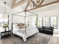 a bedroom with a bed, couch and chandelier hanging from the ceiling in front of two windows