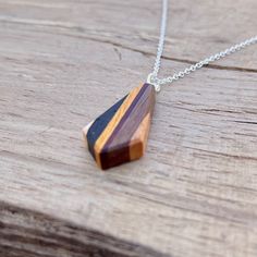 a wooden pendant on a chain sitting on top of a piece of wood and silver