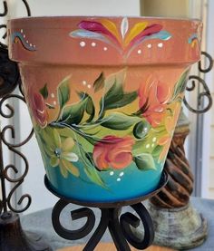 a painted flower pot sitting on top of a wooden table next to a metal stand