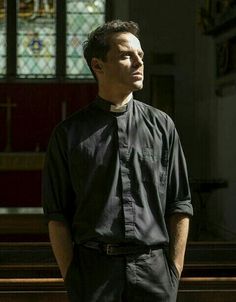 a man standing in front of a church pew with his hands in his pockets and looking off to the side