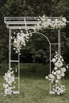 an outdoor wedding ceremony with white flowers on the arch and greenery in the background