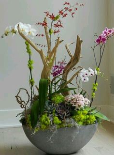 a bowl filled with flowers and plants on top of a wooden floor next to a window