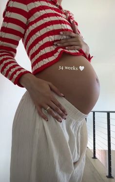 the pregnant woman is wearing a red and white striped shirt with her belly exposed,