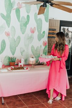 a woman in a pink dress standing next to a table with desserts on it