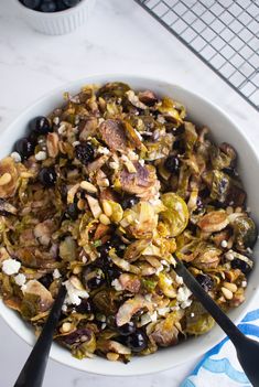 a white bowl filled with lots of food next to two spoons on a table