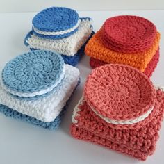 four crocheted dishcloths are sitting on a white counter top, one is blue and the other is red