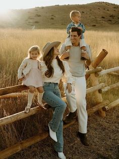 a man, woman and two children are standing on a wooden fence in the middle of a field